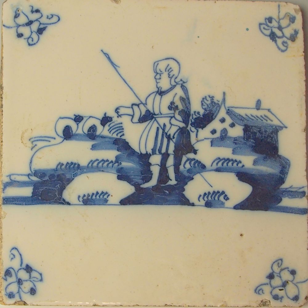 Hand-painted blue Delft tile of a man with a staff standing in a landscape beside a farmhouse